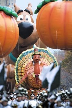 an inflatable thanksgiving turkey float is being paraded down the street with large pumpkins