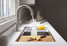 a kitchen sink filled with water and lemons next to a cutting board on the counter