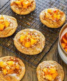 several cookies on a cooling rack with peaches next to it and a bowl of fruit in the background