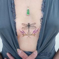 a woman's chest with a dragonfly tattoo on her left side and purple flowers in the middle