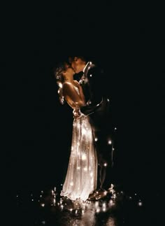 a bride and groom kissing in the dark with fairy lights on their wedding day at night