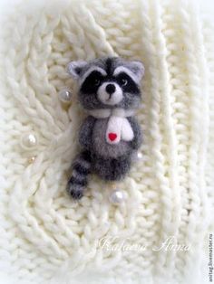 a small stuffed raccoon laying on top of a white knitted blanket with beads