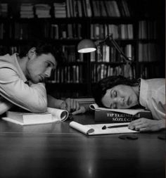 two people are sleeping on the table in front of books