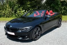 a black bmw convertible with red seats parked in front of some bushes and trees,