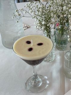 a drink in a goblet sitting on top of a table next to vases with flowers