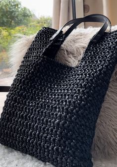 a black crocheted bag sitting on top of a white blanket next to a window