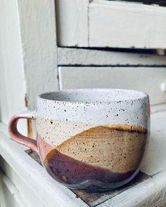 a white and brown cup sitting on top of a wooden table next to a door