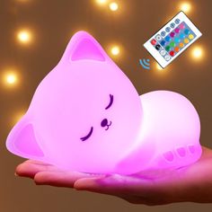 a hand holding a pink light with a remote control on it and a cat lamp in the background