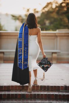 a woman wearing a graduation gown and holding a black and blue stole walking up some steps