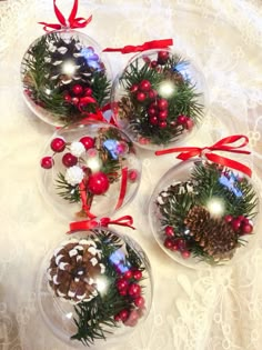 three glass ornaments with pine cones, berries and other decorations are on a lace tablecloth