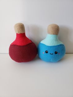 two stuffed animals sitting next to each other on a white surface with one red and one blue