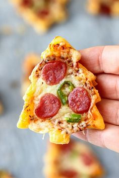 a slice of pizza with pepperoni, green peppers and cheese is held up to the camera