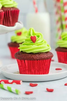 chocolate cupcakes with green frosting on a white plate next to red and green sprinkles