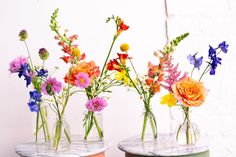 three vases filled with colorful flowers on top of marble bases in front of a white wall