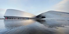 people walking on the water in front of a large building that is shaped like a boat