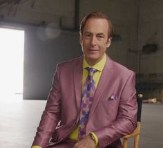 a man sitting in a chair wearing a purple suit and yellow shirt with polka dot tie