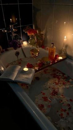 a bathtub filled with candles and rose petals next to a book on the floor