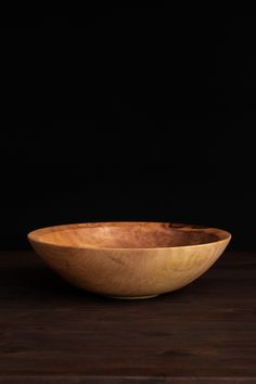 a wooden bowl sitting on top of a wooden table next to a black wall in the background