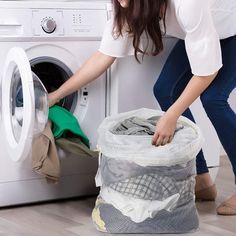 two women loading clothes from a washing machine into a laundry bag in front of a dryer