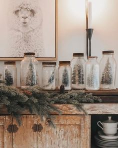 there are many glass jars on the mantle with pine branches in front of them and a lit candle