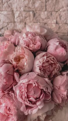 a bouquet of pink peonies in front of a brick wall