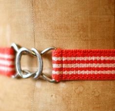 a red and white striped belt with two metal hooks on the side, attached to a tan fabric