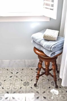 towels are stacked on top of an old stool in the corner of a bathroom with a window