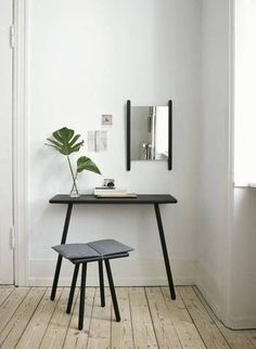 a black table with a mirror and a plant on it next to a stool in a white room