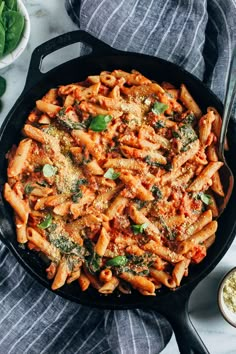 a skillet filled with pasta and spinach on top of a white countertop