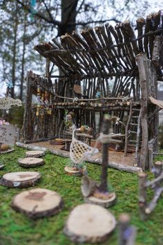 a miniature house made out of sticks and logs on top of green moss covered ground