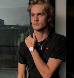 a young man standing in front of a window with his hand on his chin and looking off to the side