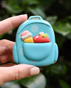 a hand holding a small blue backpack shaped toy