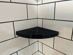 a black shelf in the corner of a white tiled wall with black grouting