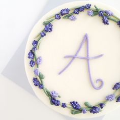 a white cake with purple flowers on it and the letter'a'in the middle