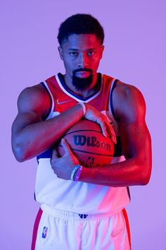 a man holding a basketball in his right hand and posing for a photo on a purple background