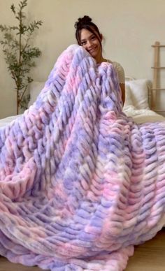 a woman sitting on the floor under a large purple and pink knitted throw blanket