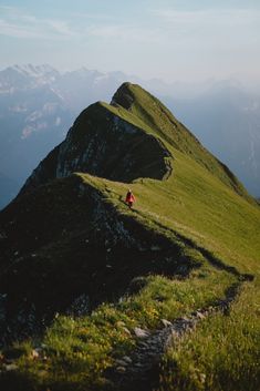 a person walking up the side of a mountain on top of a grass covered hill