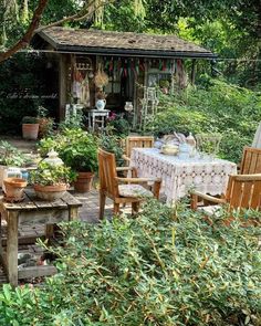 an outdoor table and chairs in the middle of a garden with lots of greenery