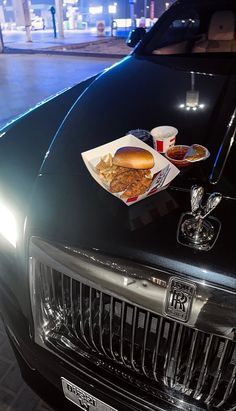 a grilled sandwich and drink sit on the hood of a black sports utility vehicle