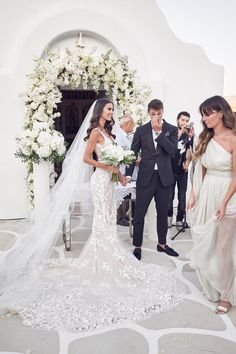 a bride and groom standing in front of an arch with white flowers on the side