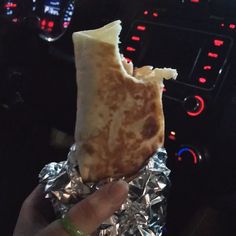 a person holding up a piece of food in foil on the dashboard of a car