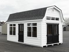 a small white building with black doors and windows on the roof is in an empty lot