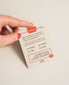 a hand holding an animal business card on top of a white surface with orange lettering