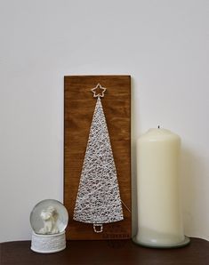 a wooden plaque with a white christmas tree on it next to a candle and a glass ball