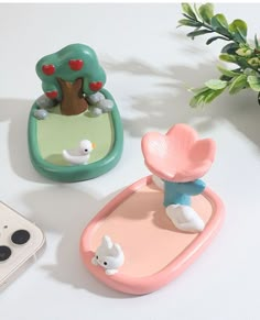 two small figurines sitting on top of a table next to a cell phone