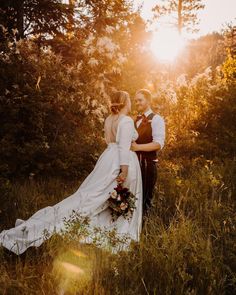 a bride and groom standing in tall grass with the sun shining through the trees behind them