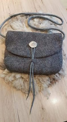 a gray purse sitting on top of a pile of sheep fur next to a wooden floor