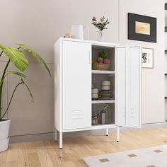 a white cabinet sitting on top of a wooden floor next to a potted plant