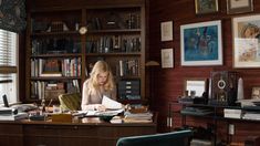 a woman sitting at a desk in front of a bookshelf filled with books