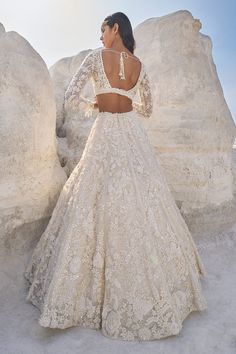 a woman standing in front of some rocks wearing a wedding dress with an open back